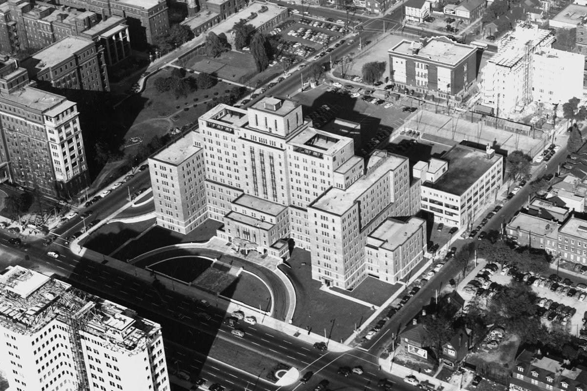 Historic aerial black and white photograph of a large hospital complex with surrounding urban buildings and streets.RetryClaude can make mistakes. Please double-check responses.